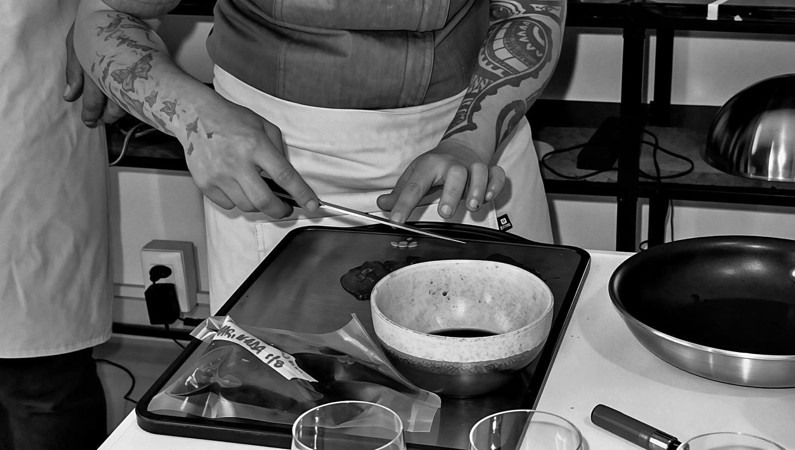 Cook in an apron drawing a knife across a tray beside a stone bowl and pan