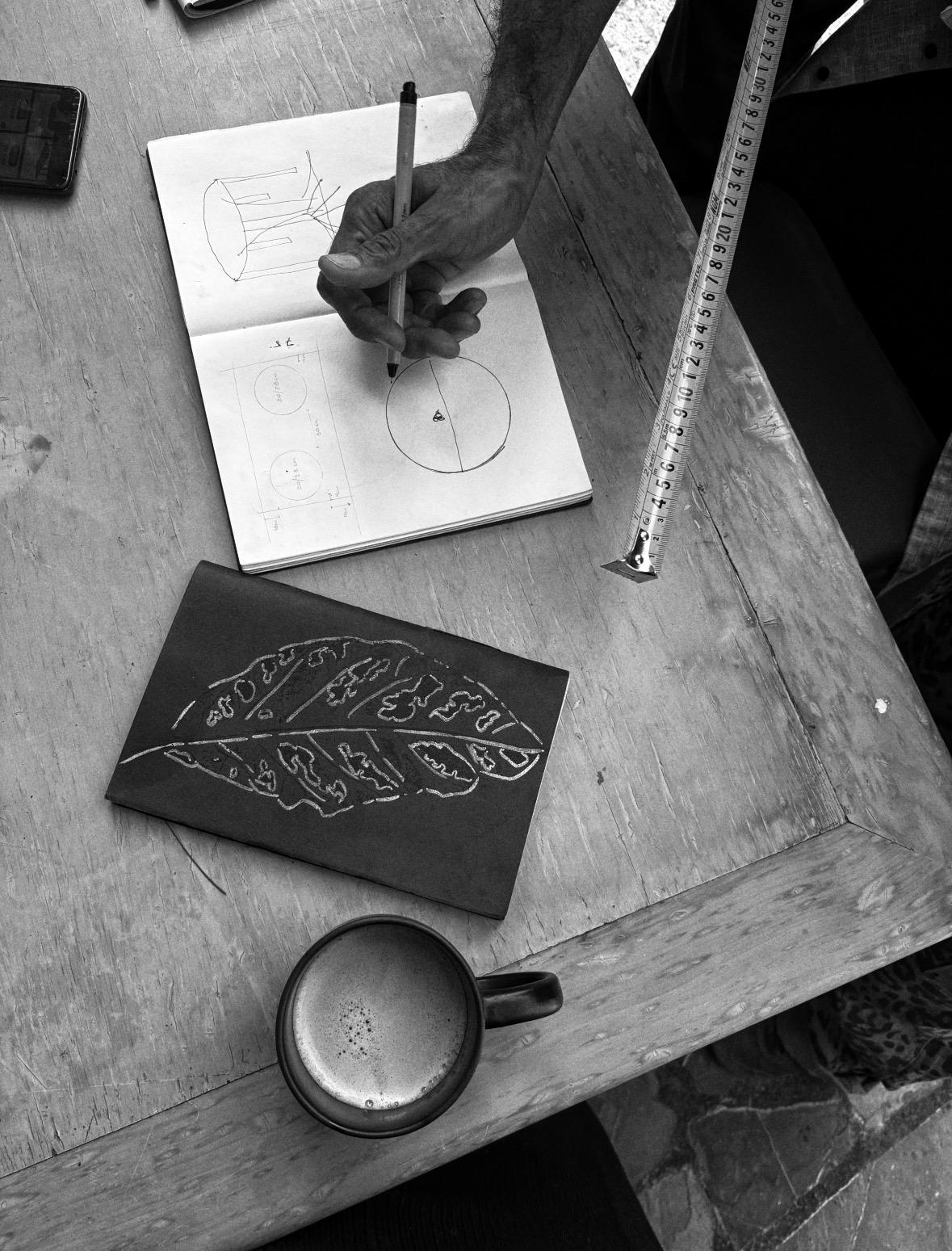 Hand sketching in a notebook beside a carved linocut block and tape measure