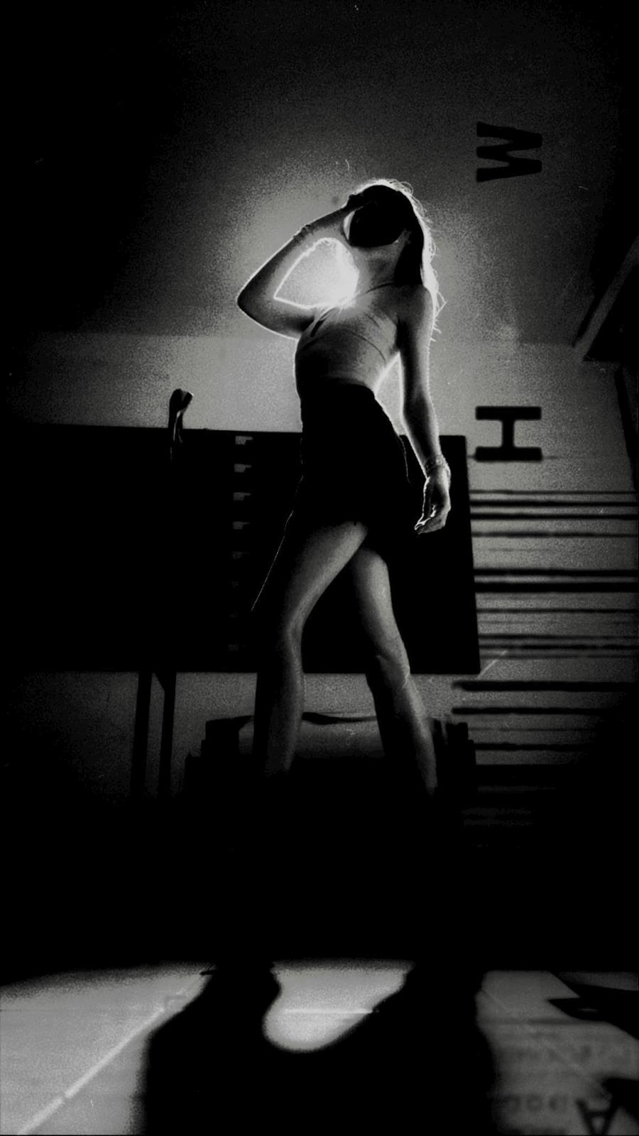 Backlit figure standing in a darkened room, lettering on the wall behind