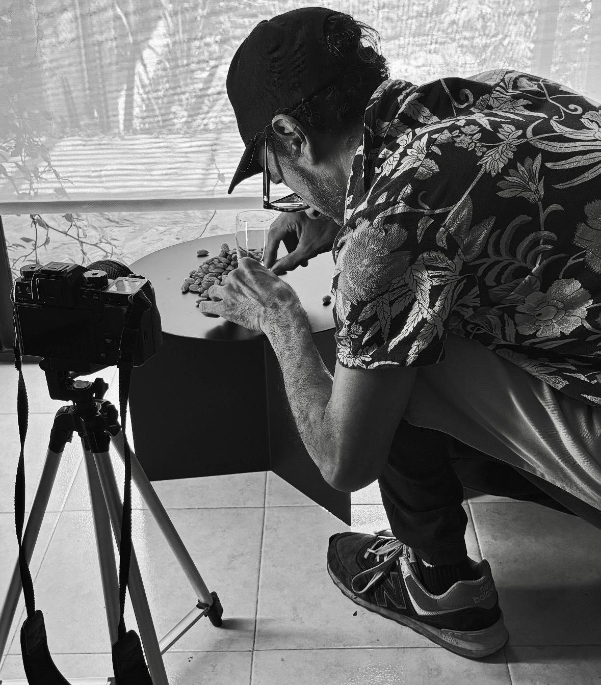 Photographer crouched over a low table, shooting seeds beside a camera on a tripod